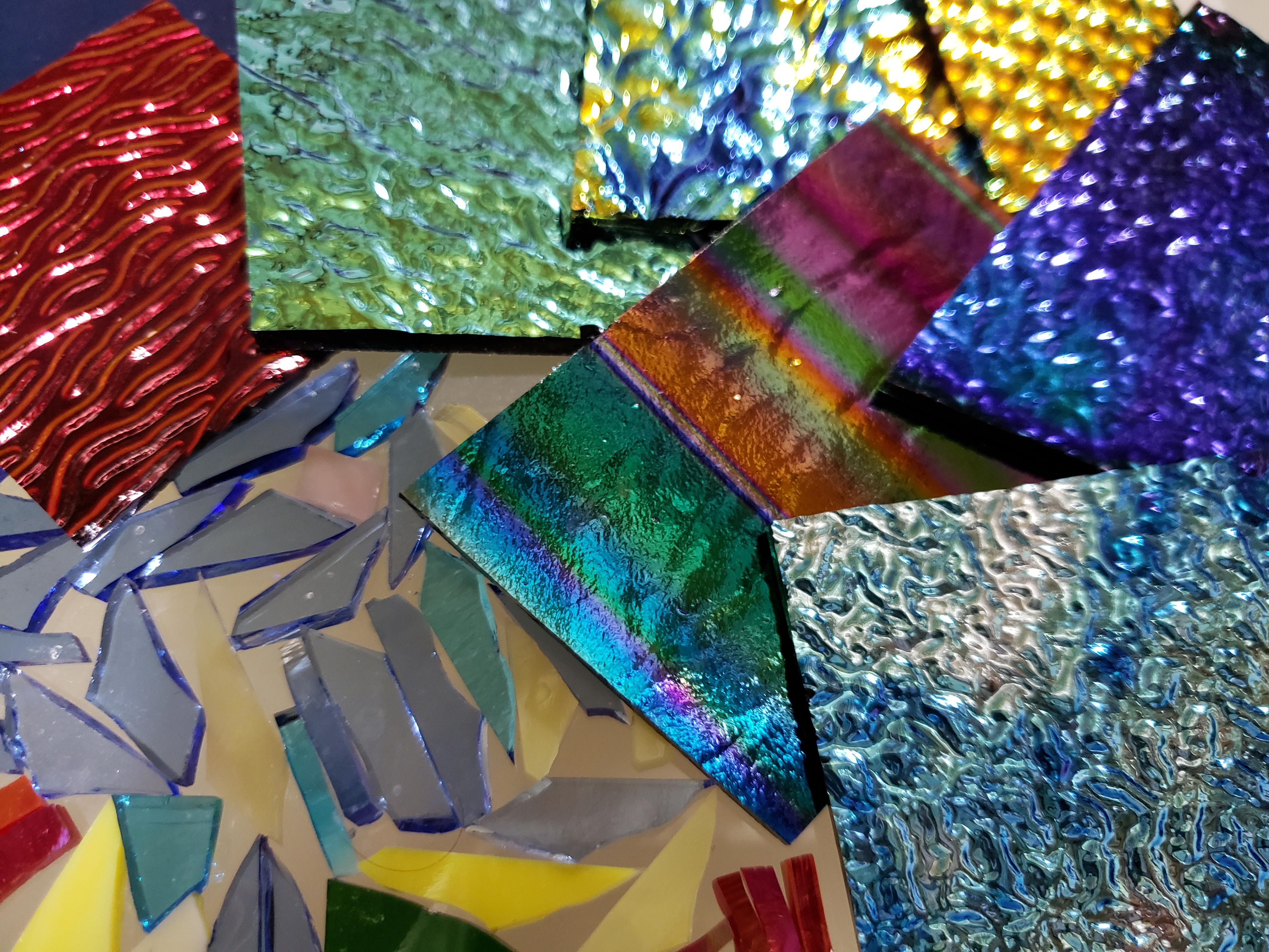 Various colourful pieces of stained glass sit on a wooden workshop table.