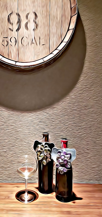 Two wine bottles with white and purple grape wine charms sit on a table, next to a glass of white wine. 